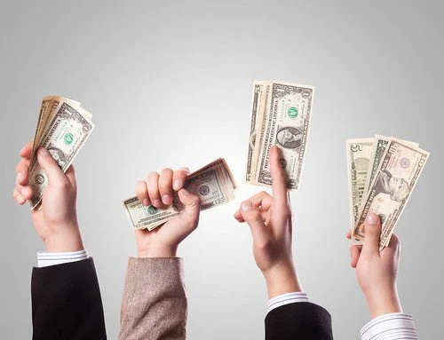 4 people's hands hold US dollar bills in the air