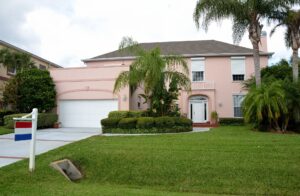 A View of A Pink House With A Front Yard That Has Palm Trees, Bushes, and Green Grass