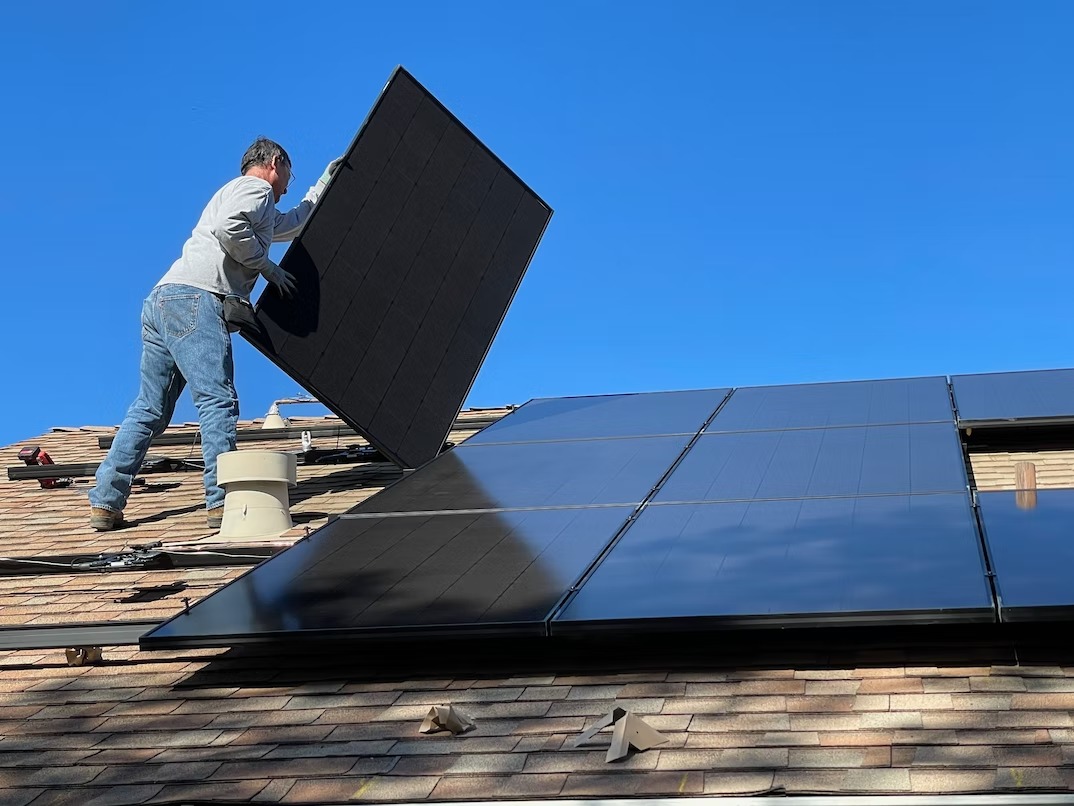 A worker installing a solar panel on a roof