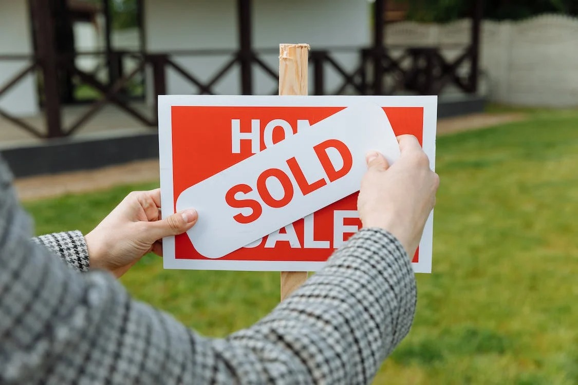 Person holding a "sold" sign on top of a home for sale sign